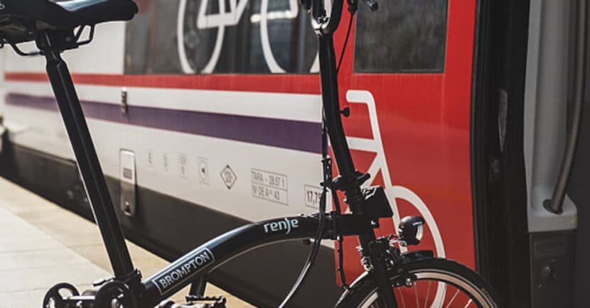 Una de las bicicletas Brompton con el logo de Renfe junto a un tren de Cercanías. © RENFE.
